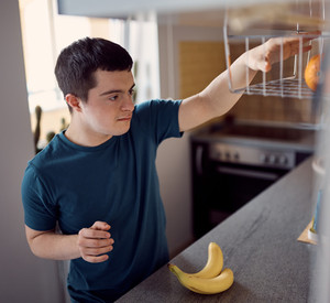 Junger Mann mit Down-Syndrom, der Obst für den Snack in der Küche nimmt