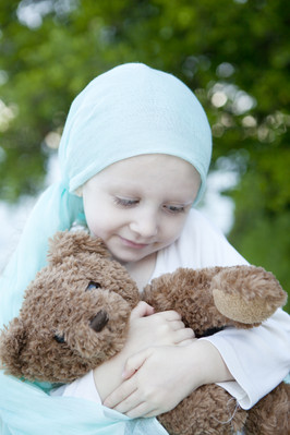 Krebskrankes Mädchen hält Teddy im Arm