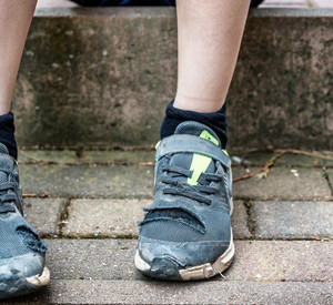 Unkenntliches Kind sitzt mit kaputten Schuhen auf Gehweg