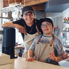 Ein Kind mit einer Behinderung steht zusammen mit einem Mann hinter einem Tresen eines Cafés