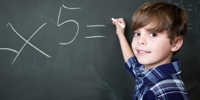 Ein kleiner Junge schreibt mit Kreide die Lösung einer Mathematikaufgabe an die Schultafel.