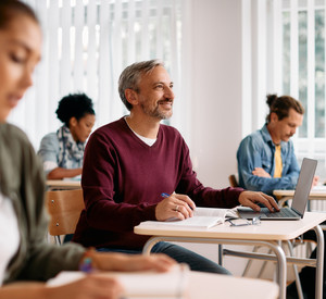 Älterer Mann sitz in einem Seminar am Schreibtisch mit Laptop
