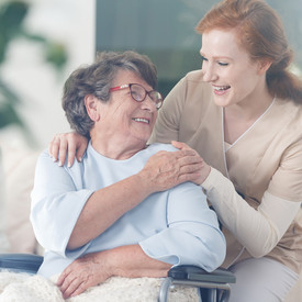 Junge Frau umarmt Seniorin, die in einem Rollstuhl sitzt