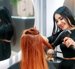 Junge Friseurin föhnt Kundin die Haare