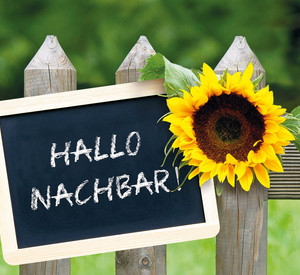 Schild an Gartenzaun mit der Aufschrift Hallo Nachbar!