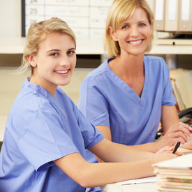 Eine Krankenschwesternschülerin neben Lehrerin am Schreibtisch