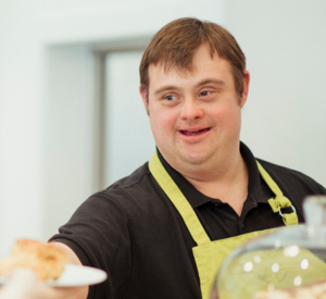 Ein Mann mit Downsyndrom überreicht Kuchen an eine Person