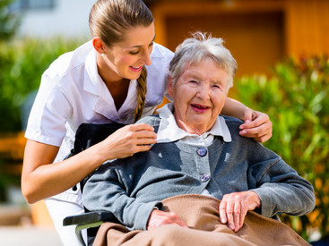 Seniorin im Rollstuhl wird von Pflegekraft umarmt