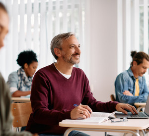 Älterer Mann sitz in einem Seminar am Schreibtisch mit Laptop.