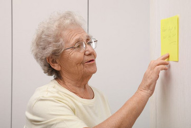 Seniorin liest einen Zettel, der an der Wand klebt