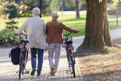 Seniorenpaar mit Fahrrädern, die gemeinsam durch den Park laufen