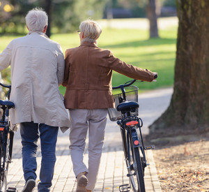 Seniorenpaar mit Fahrrädern, die gemeinsam durch den Park laufen