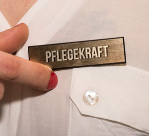 Eine Frau hält ein Namensschild mit Hinweis auf Pflegekraft