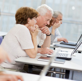 Ältere Menschen sitzen in einem Schulungsraum und haben Laptops vor sich stehen