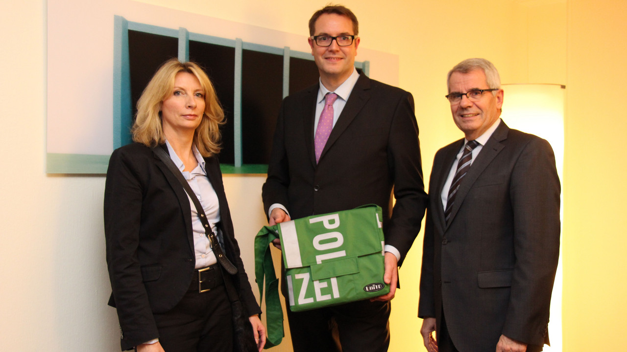 Polizeipräsident Karl-Heinz Weber und Heike Rowohlt übergeben eine Polizeitasche an Sozialminister Alexander Schweitzer